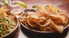 video of a dinner table with a plate of tortilla chips, guacamole dip, and beverages